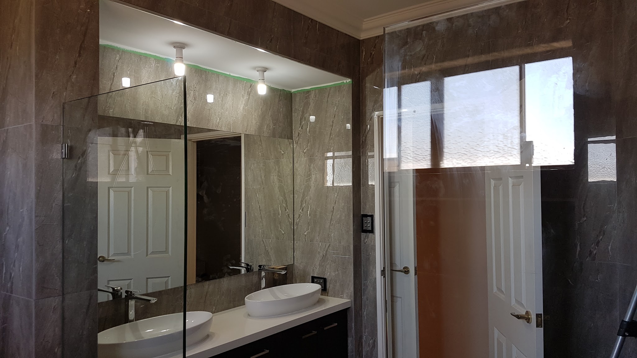 A finished bathroom with a frameless shower screen and a full width vanity mirror
