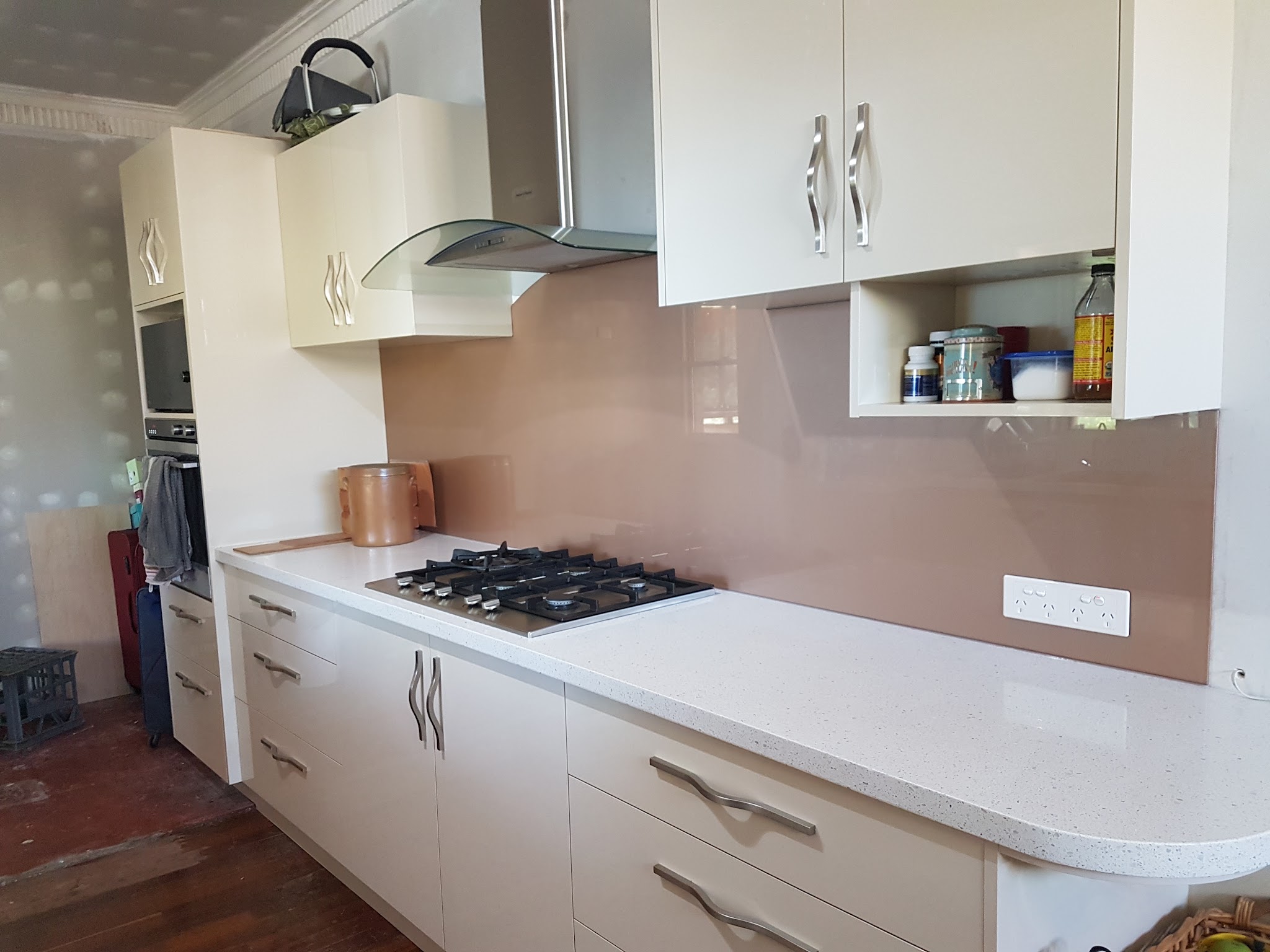 A kitchen with a mocha coloured toughened glass splashback behind a gas cooktop