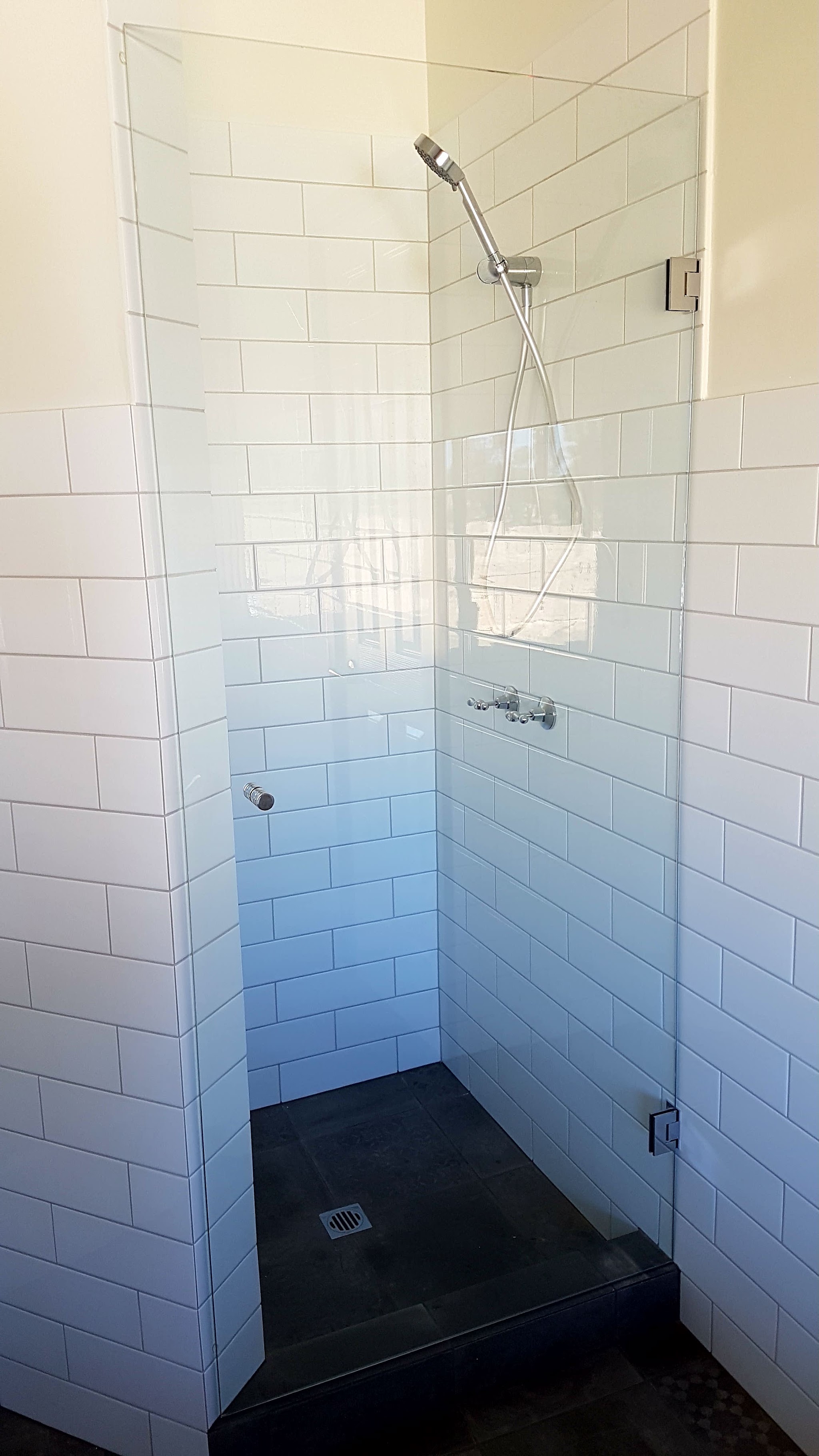A frameless glass shower screen fitted against white subway tiling