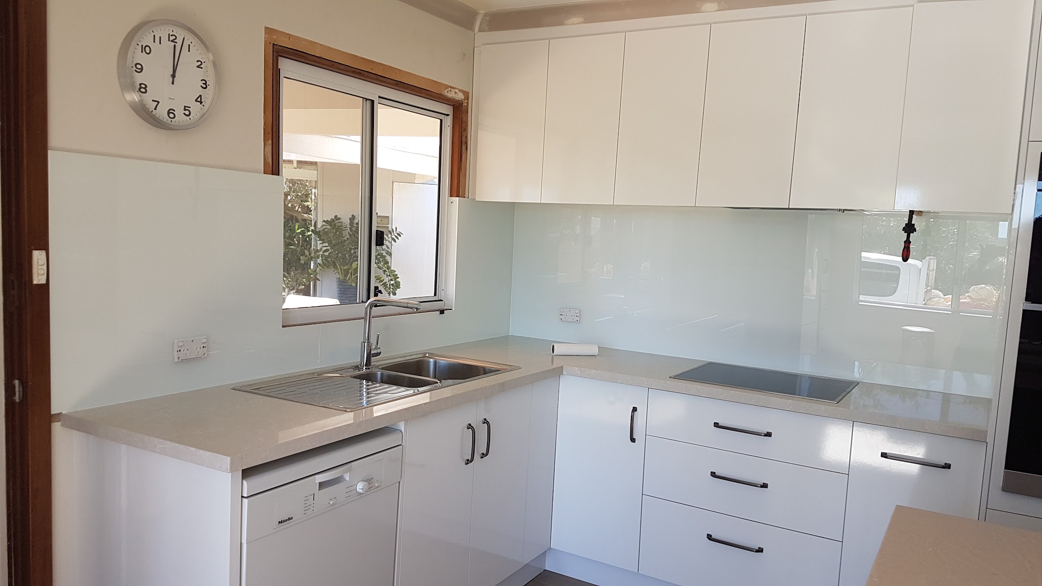 A kitchen with a pale sea glass splashback wrapping around a corner